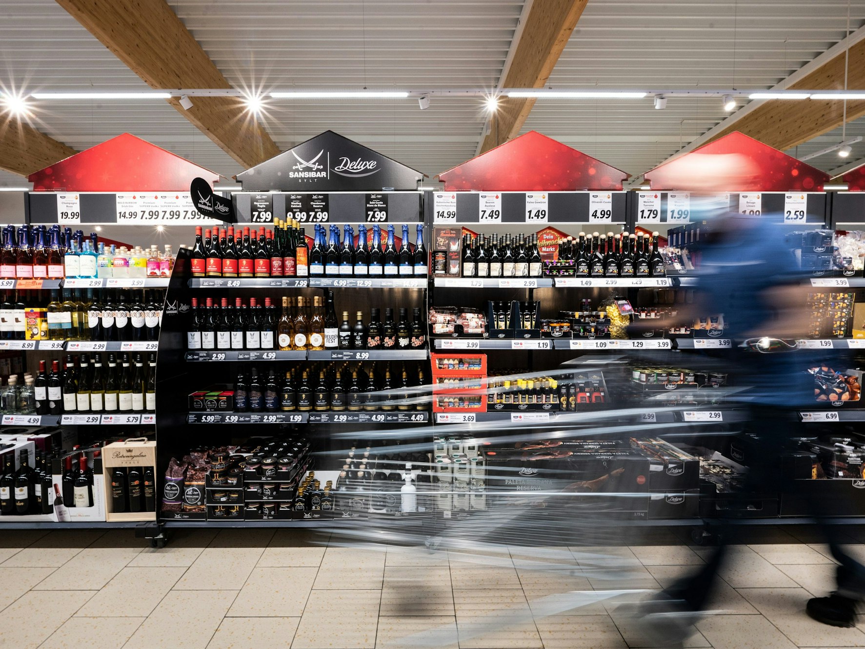 Ein Mann geht mit seinem Einkaufswagen in einer Lidl-Filiale an Regalen mit Sansibar und Deluxe-Produkten vorbei.