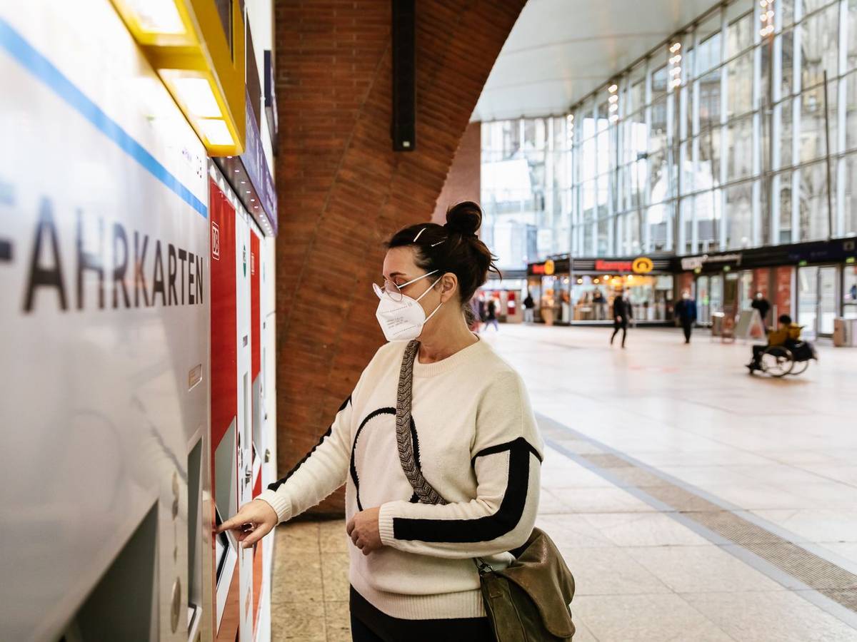 Eine Frau mit Maske zieht sich im Kölner Hauptbahnhof ein Ticket aus einem VRS-Automaten.