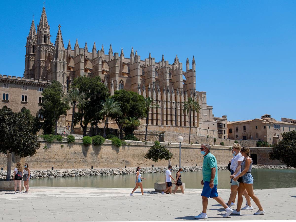 Touristen und Touristinnen gehen vor der Kathedrale von Palma auf Mallorca entlang. Die Aufnahme dient als Symbolfoto.