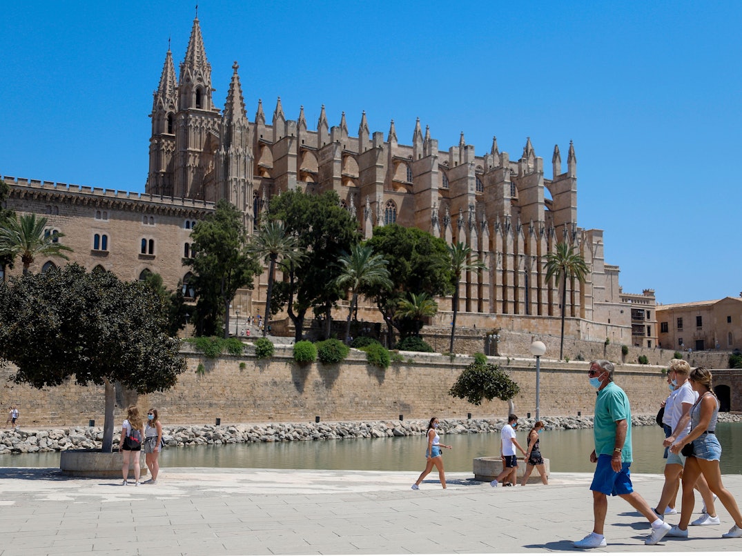 Touristen und Touristinnen gehen vor der Kathedrale von Palma auf Mallorca entlang. Die Aufnahme dient als Symbolfoto.