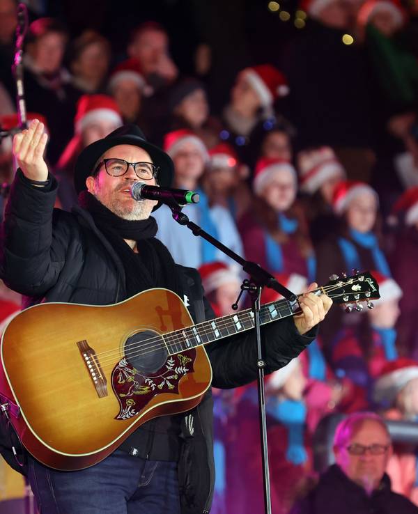 Ein Mann mit Gitarre steht vor zahlreichen Menschen, die eine Weihnachtsmann-Mütze tragen.