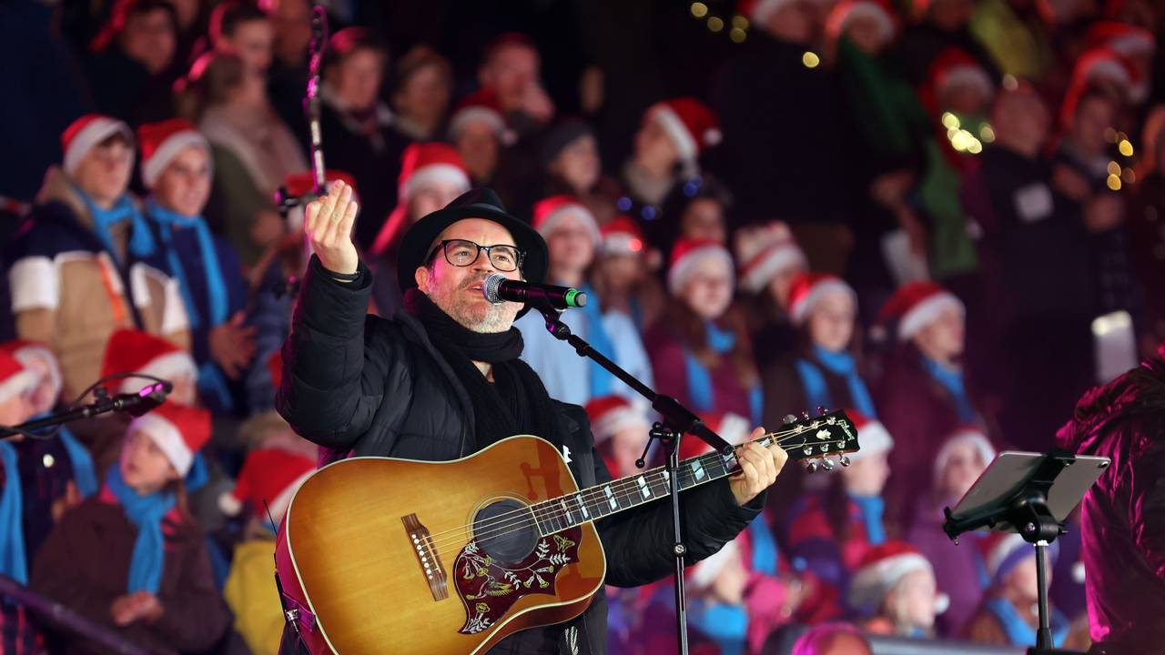Ein Mann mit Gitarre steht vor zahlreichen Menschen, die eine Weihnachtsmann-Mütze tragen.