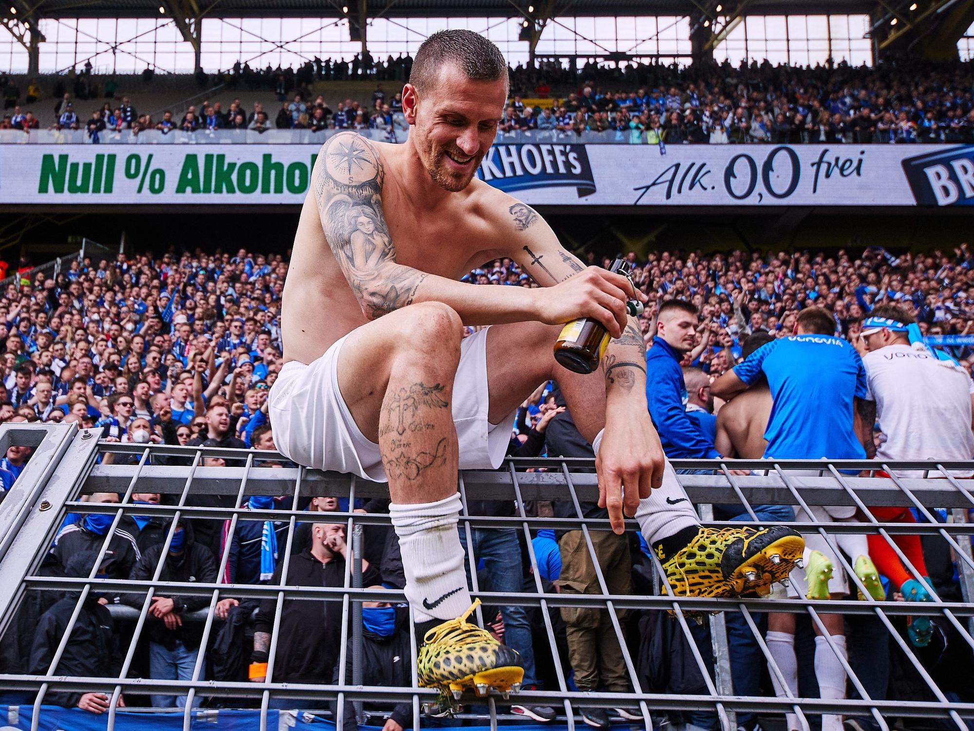 Simon Zoller sitzt nach dem 4:3-Sieg bei Borussia Dortmund auf dem Zaun vor dem Fan-Block des VfL Bochum.