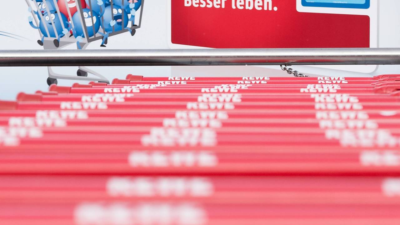 Vor einem Schild, das die Rewe-Paybackkarte zeigt, stehen Einkaufswägen der Supermarktkette.