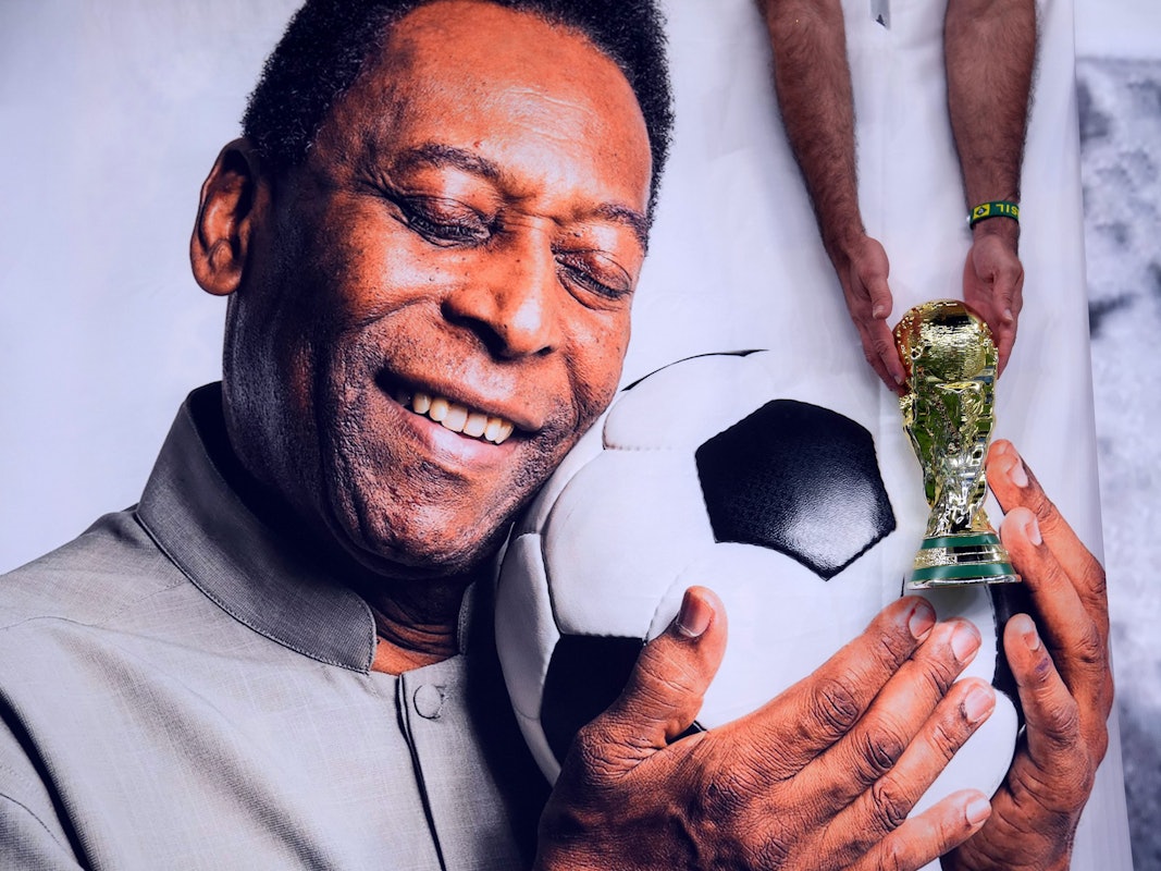 Lusail Stadion in Katar: ein brasilianischer Fan hält vor dem Spiel eine nachgebildete WM-Trophäe neben das Bild des ehemaligen brasilianischen Nationalspielers Pelé.