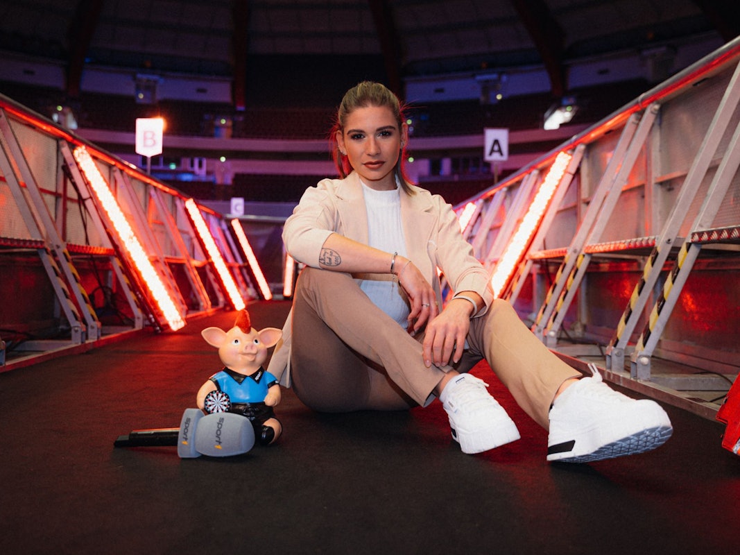 Sport1-Moderatorin Jana Wosnitza sitzt im Alexandra Palace vor der Bühne.