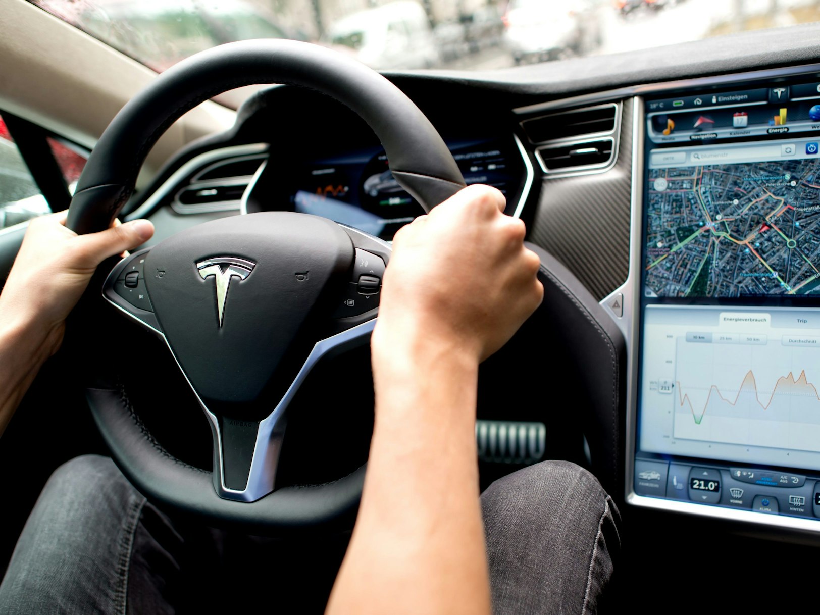 Ein Mann sitzt in einem Tesla Model S am Lenkrad, neben ihm ein großer Monitor im Armaturenbrett.