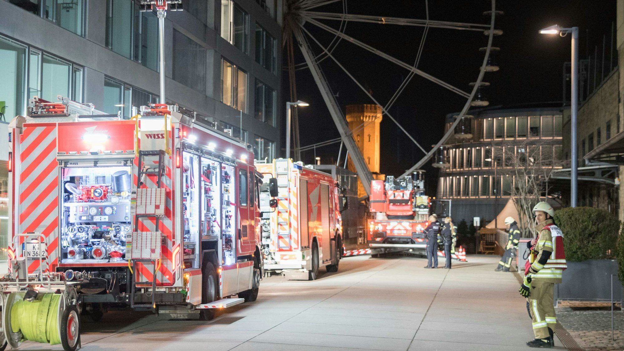 Einsatzfahrzeuge der Feuerwehr stehen vor einem mehrstöckigen Haus, im Hintergrund ist ein Teil eines Riesenrades zu sehen.