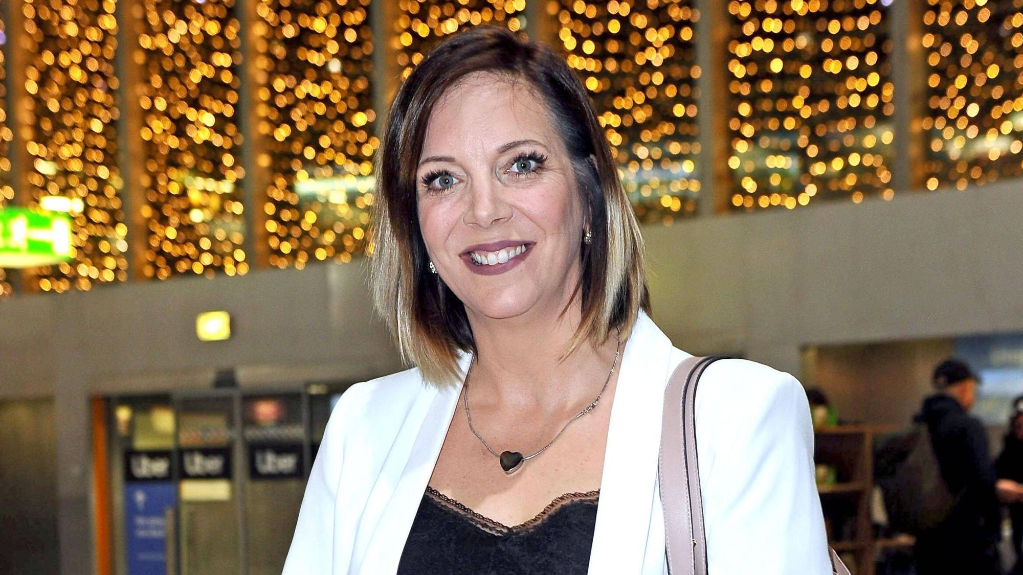 Danni Büchner lächelt am Frankfurter Flughafen in die Kamera. Sie trägt ein schwarzes Oberteil und einen weißen Blazer.
