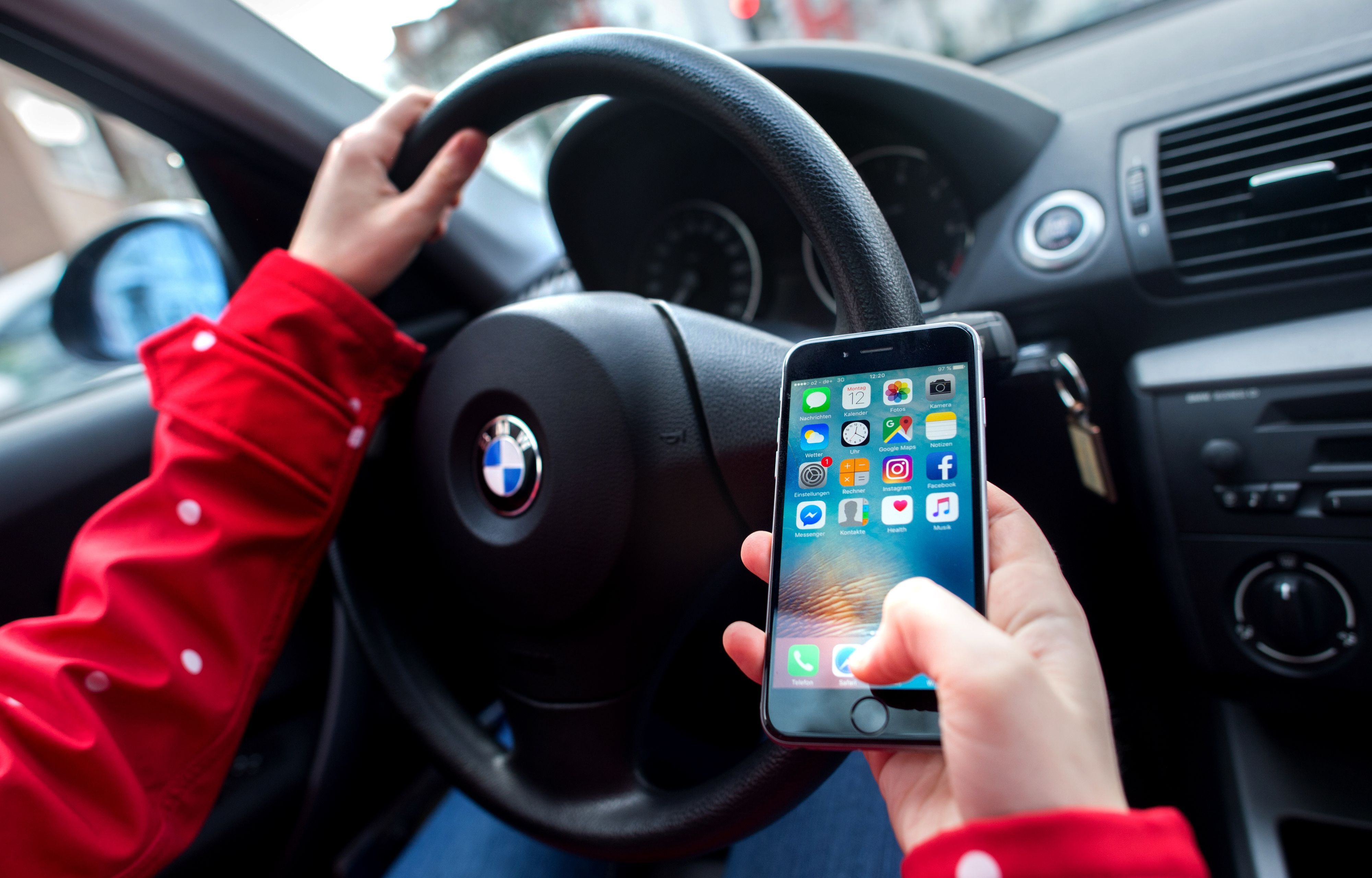 Eine junge Frau sitzt in einem Auto am Steuer und bedient dabei ihr Smartphone.