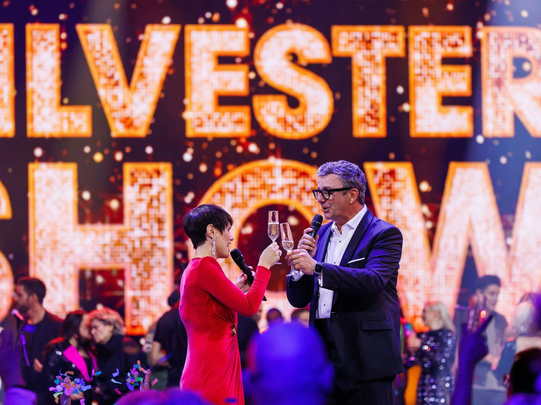 Die Moderatoren Francine Jordi (l) und Hans Sigl (r) stehen auf der Bühne und stoßen mit ihren Gläsern an.