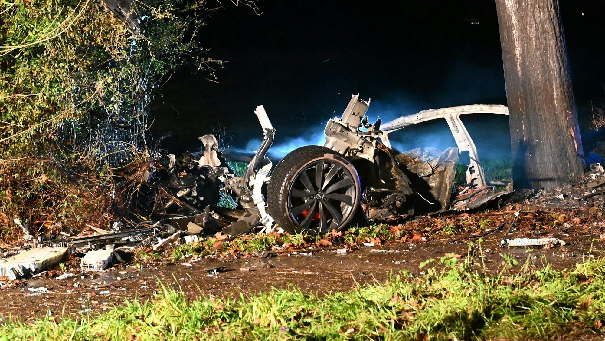 Ein in Teile zerrissenes und ausgebranntes Auto steht an einem Baum.