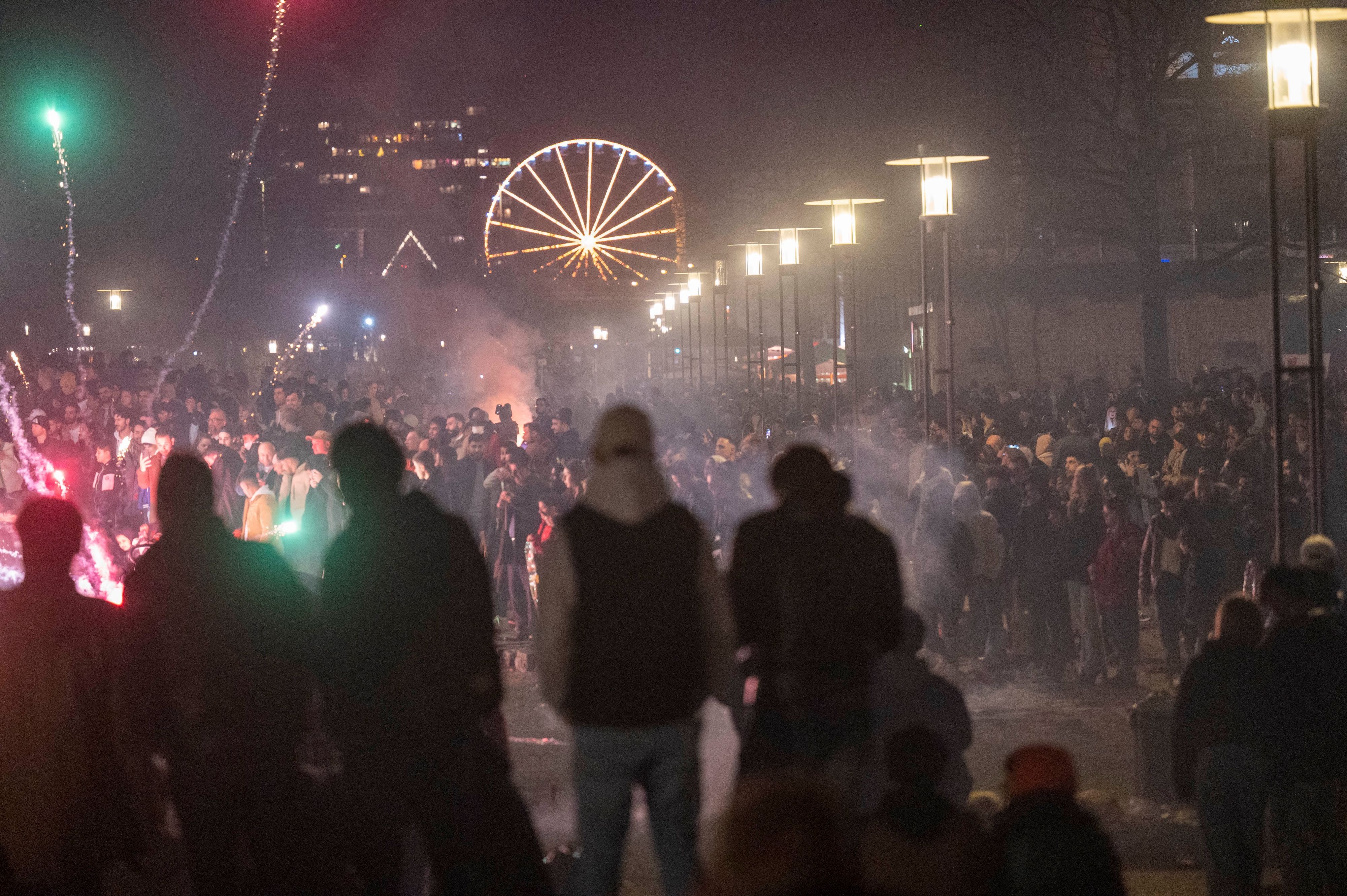 Eine große Gruppe Menschen steht in der Dunkelheit und zündet an Silvester Raketen und Böller an.