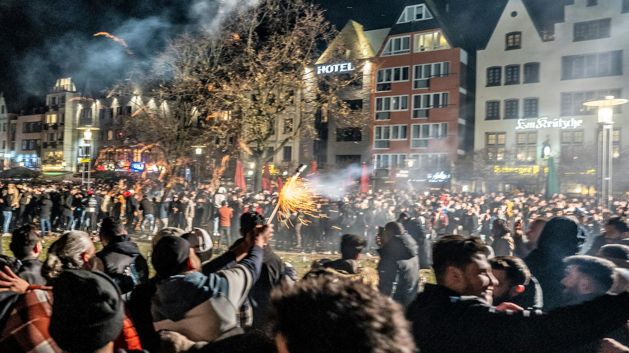 Hunderte Menschen stehen in Köln auf einer großen Platzfläche und zünden Feuerwerk.