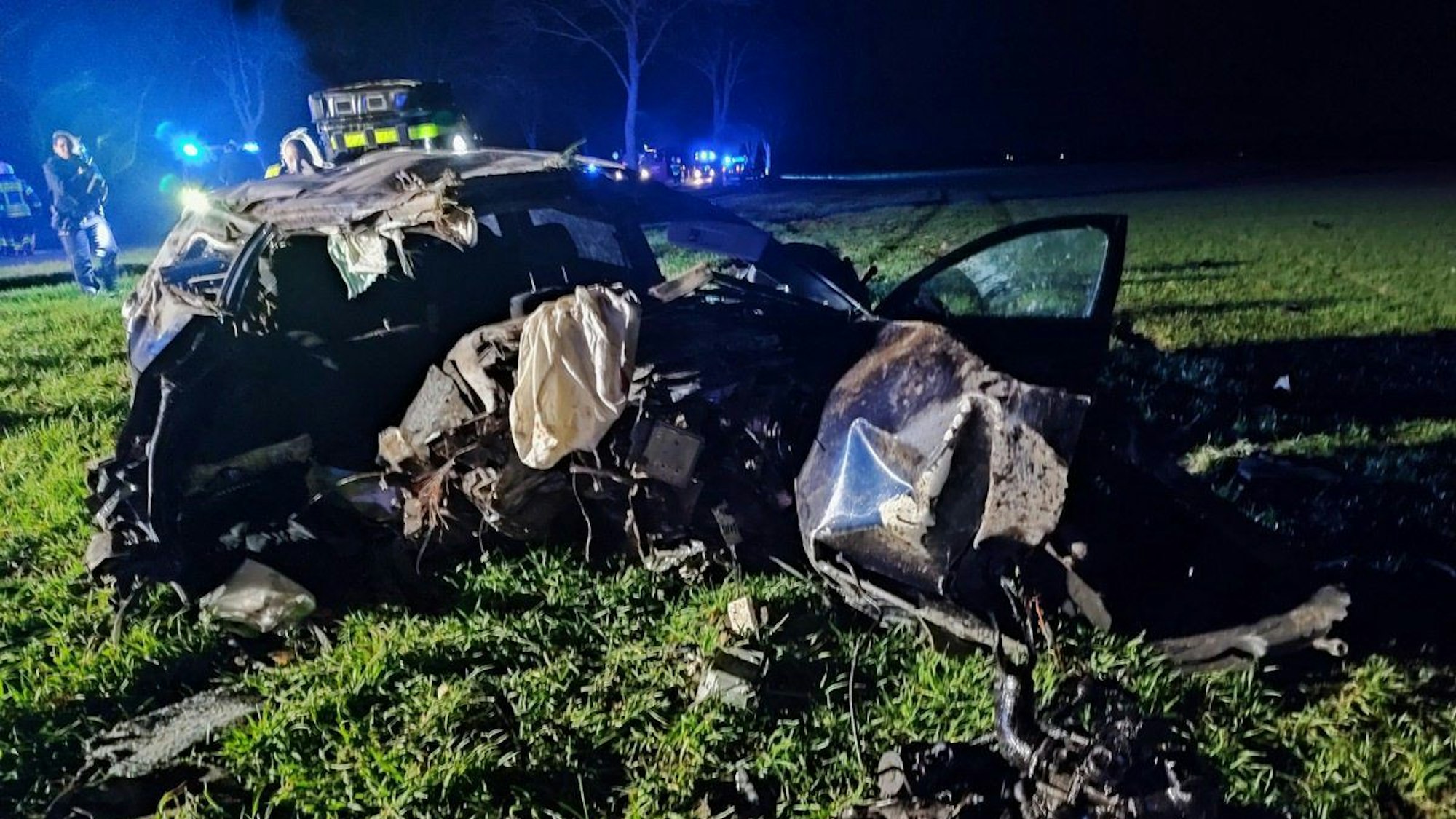 Trümmerteile eines Autos liegen auf einer Wiese.