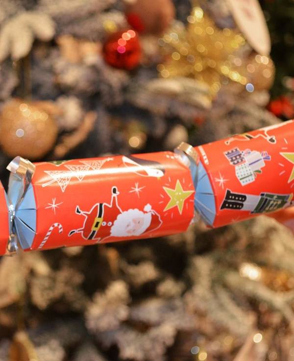 Ein Knallbonbon mit weihnachtlichen Motiven wird in den Händen gehalten.