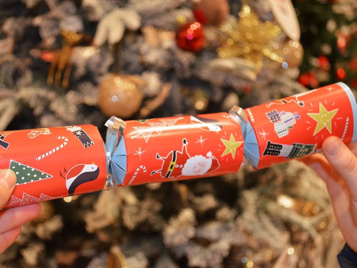 Ein Knallbonbon mit weihnachtlichen Motiven wird in den Händen gehalten.