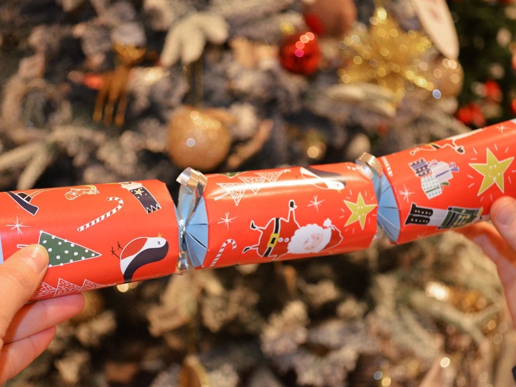 Ein Knallbonbon mit weihnachtlichen Motiven wird in den Händen gehalten.