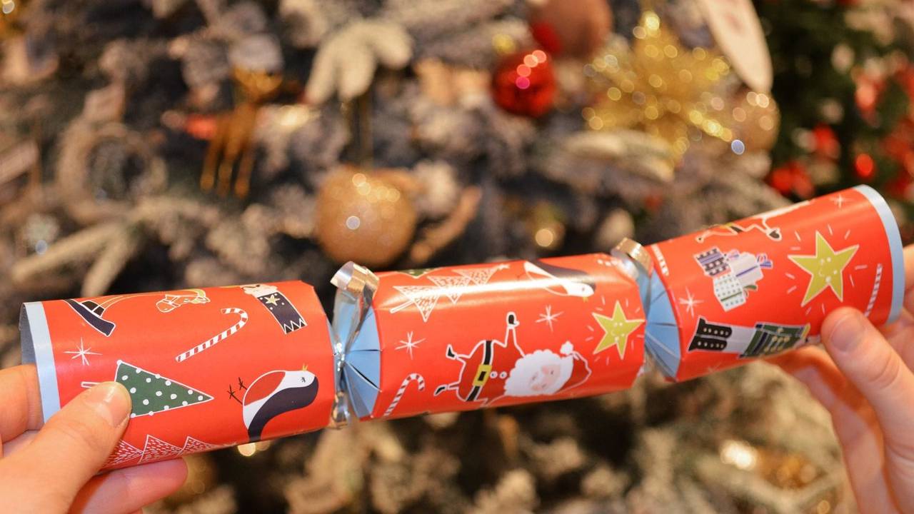 Ein Knallbonbon mit weihnachtlichen Motiven wird in den Händen gehalten.