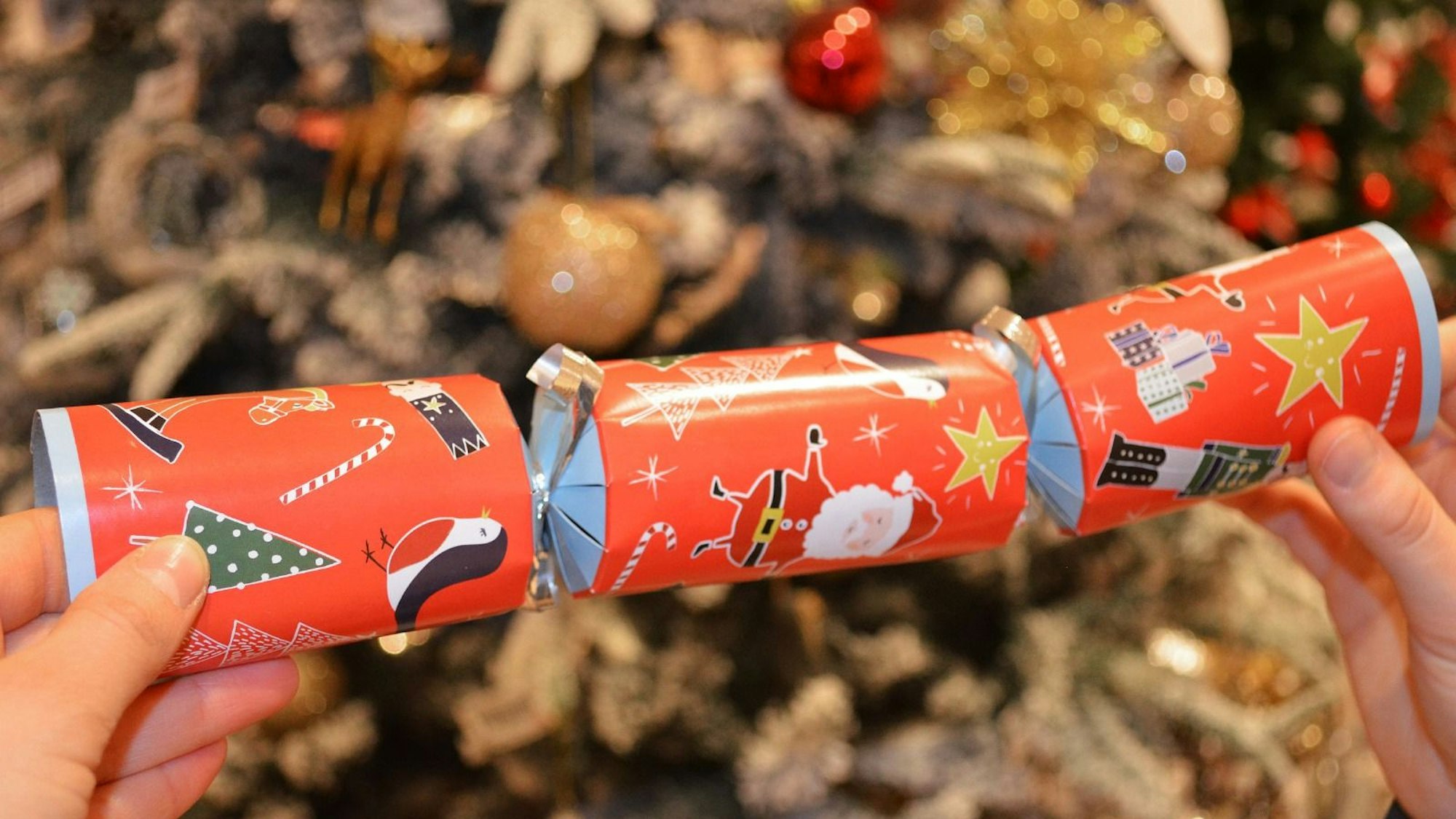 Ein Knallbonbon mit weihnachtlichen Motiven wird in den Händen gehalten.