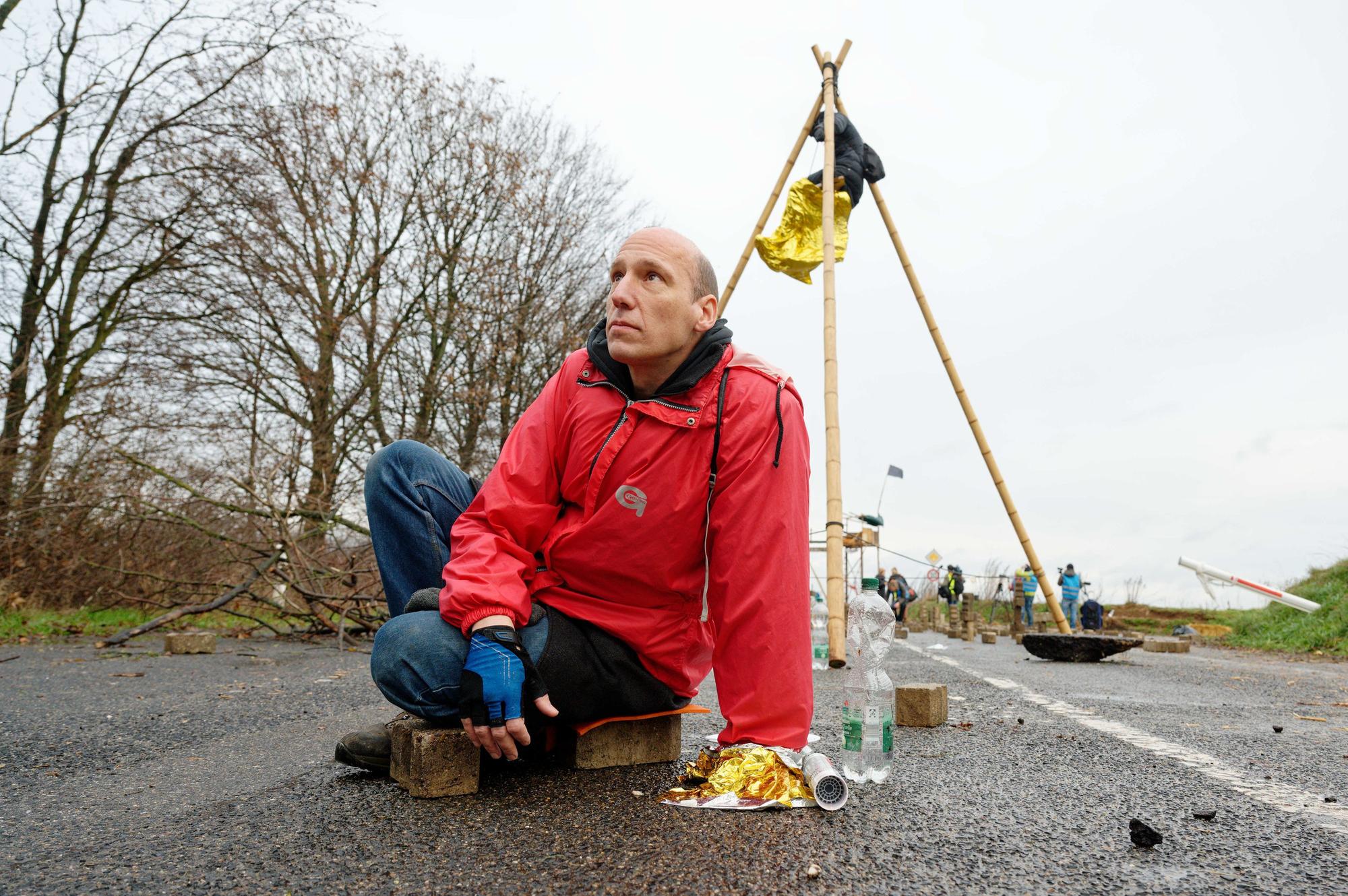 Ein Aktivist der Letzten Generation hat sich auf einer der Zufahrten in Richtung Lützerath mit einer Hand an der Straße festgeklebt.