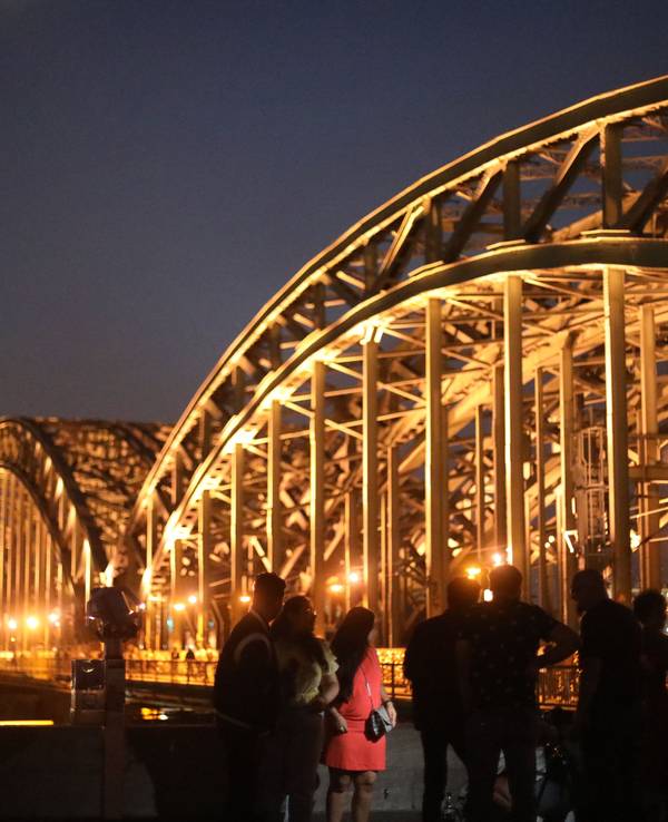 Menschen posieren vor dem Kölner Dom und der Hohenzollernbrücke am Rheinboulevard in Deutz.