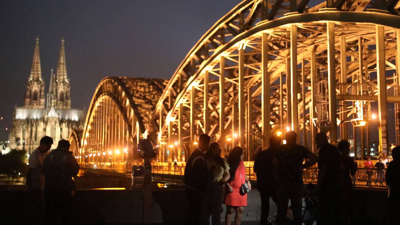 Menschen posieren vor dem Kölner Dom und der Hohenzollernbrücke am Rheinboulevard in Deutz.