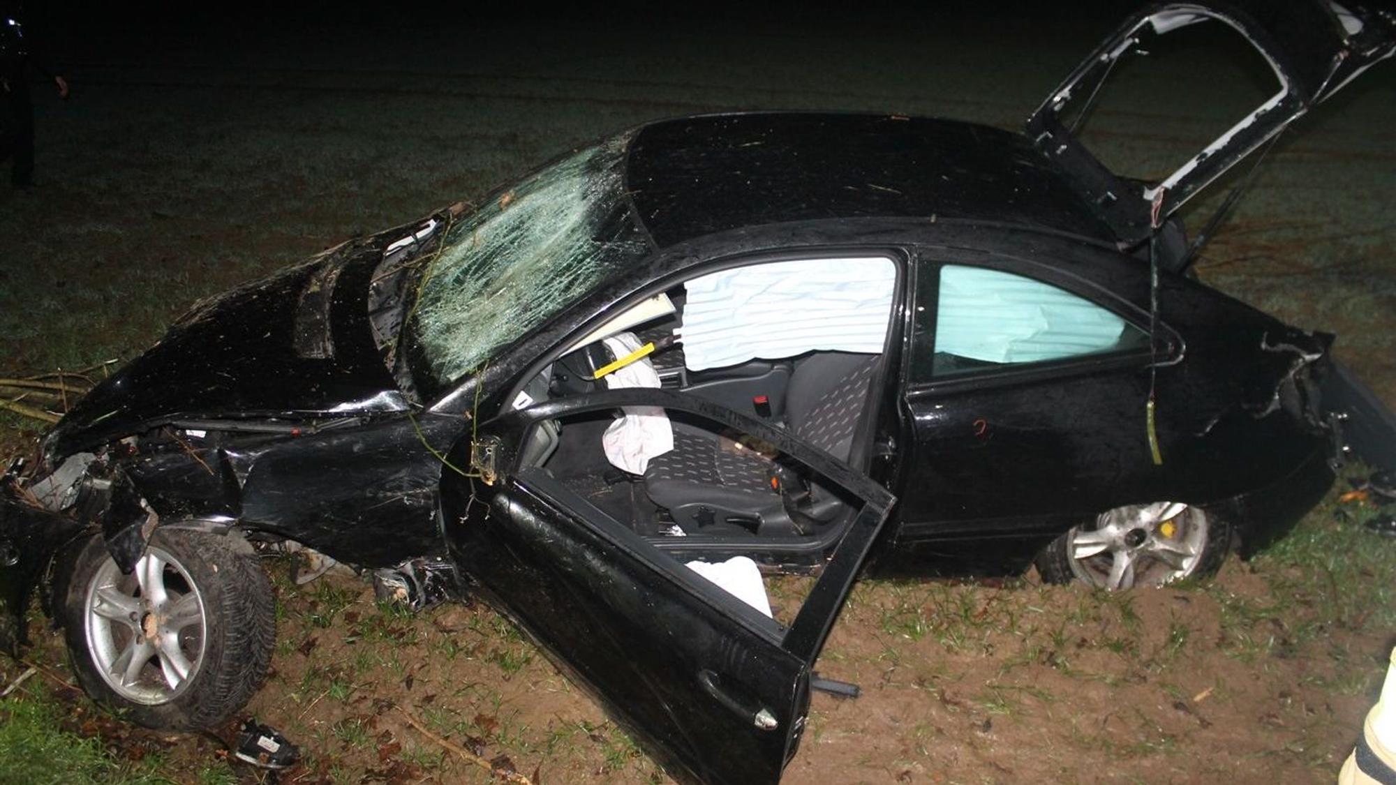 Schwer beschädigtes Auto liegt in einem Feld neben der Straße.