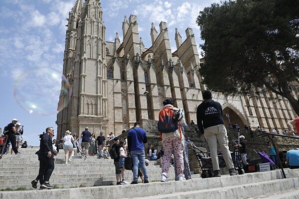 Menschen gehen neben der Kathedrale von Palma de Mallorca spazieren.