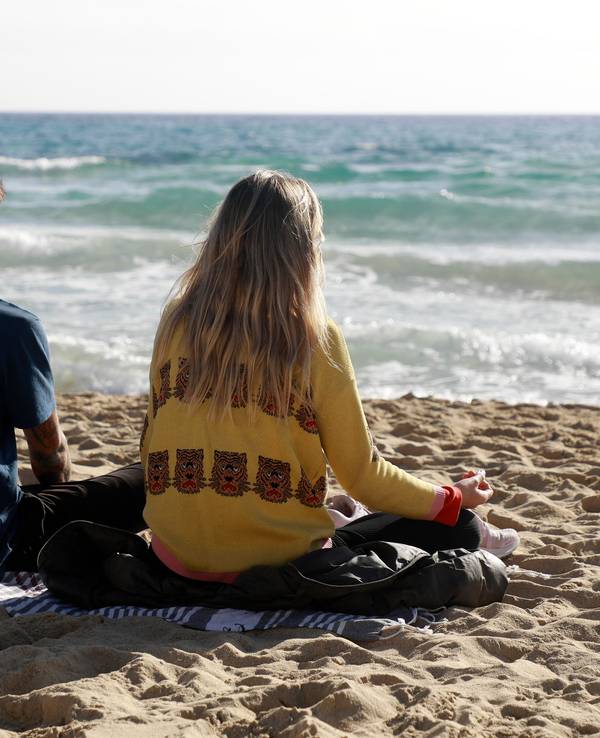 Das Foto zeigt zwei Menschen, die auf einer Decke am Strand sitzen und auf das Meer schauen.