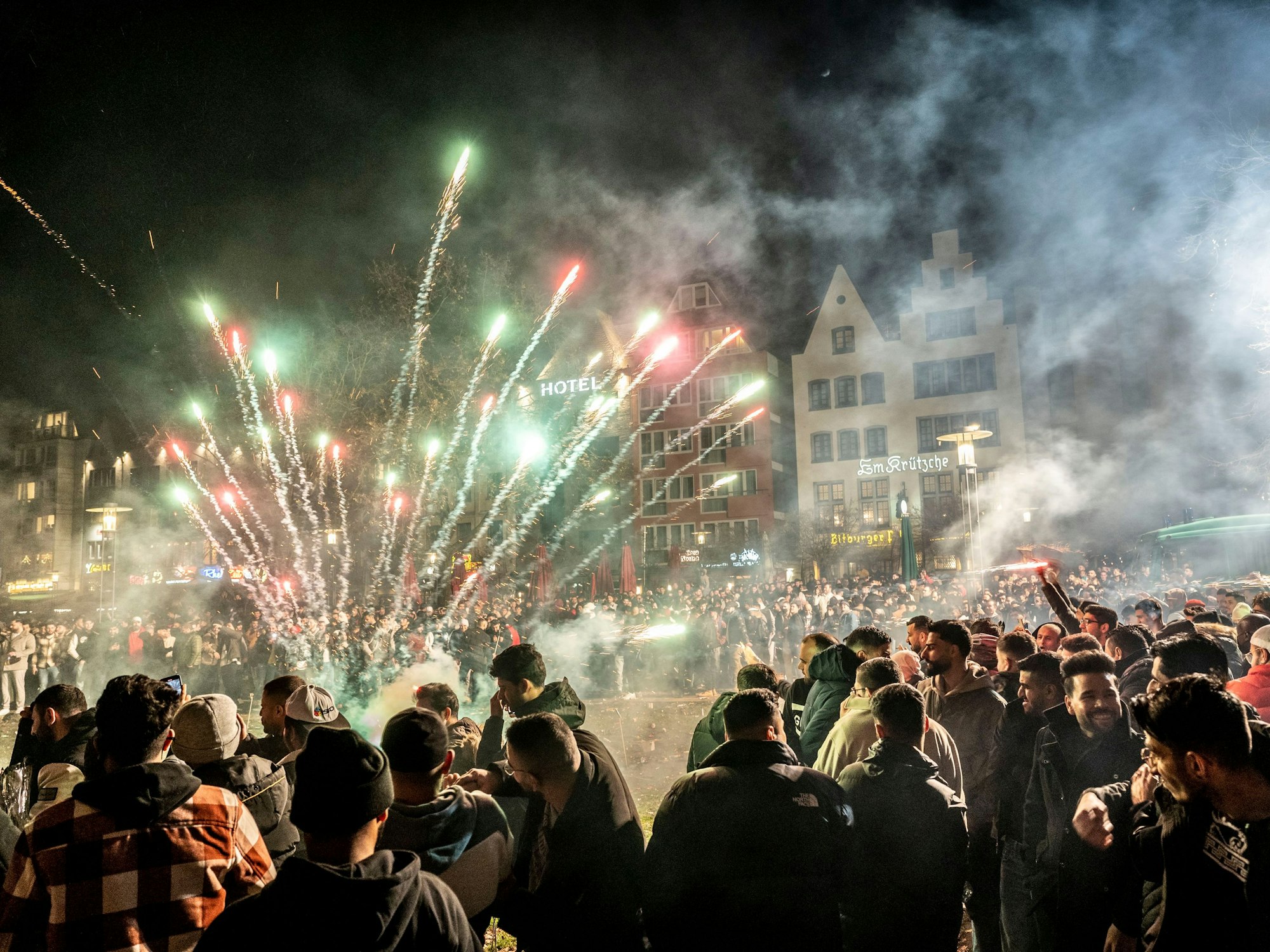 Menschen feiern in der Kölner Innenstadt den Jahreswechsel auf 2023. Auch Raketen fliegen durch die Luft.