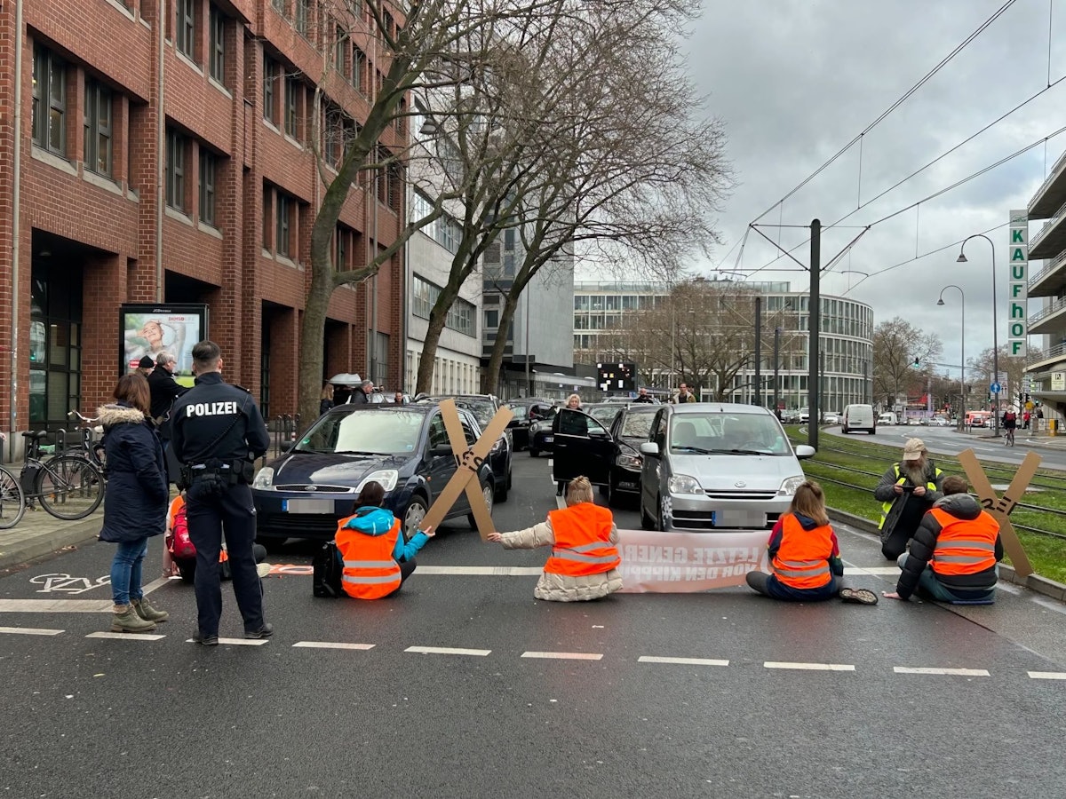 Aktivistinnen und Aktivisten der „Letzten Generation“ blockieren am Freitagmittag mit einer Sitzblockade eine der zentralen Verkehrsachsen in der Kölner Innenstadt.