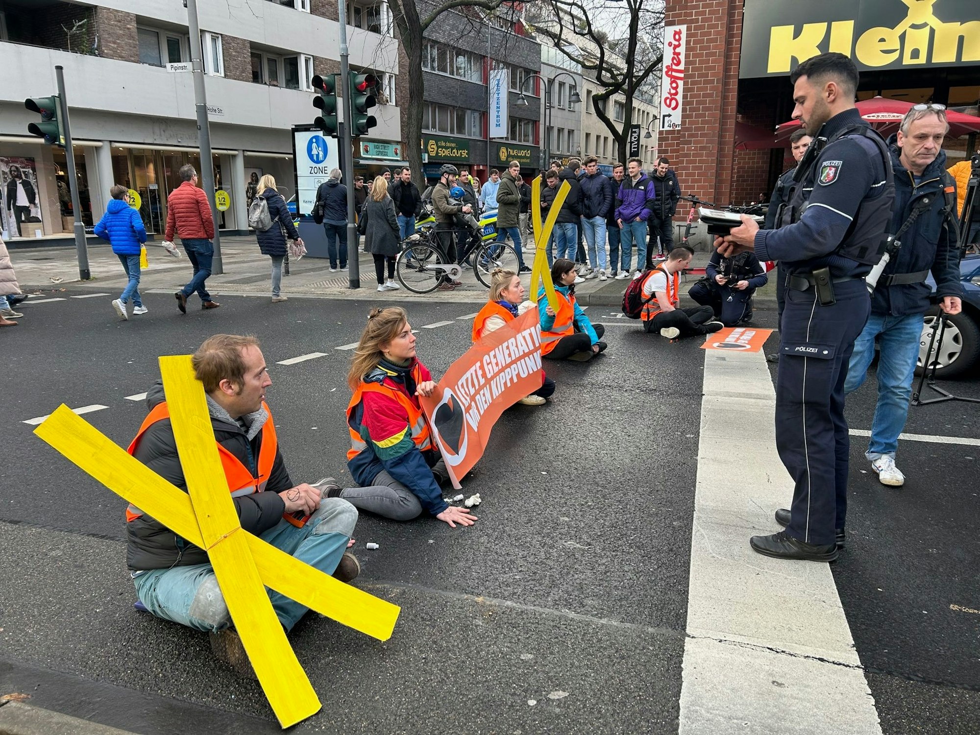 Aktivistinnen und Aktivisten der „Letzten Generation“ blockieren am Freitagmittag mit einer Sitzblockade eine der zentralen Verkehrsachsen in der Kölner Innenstadt.