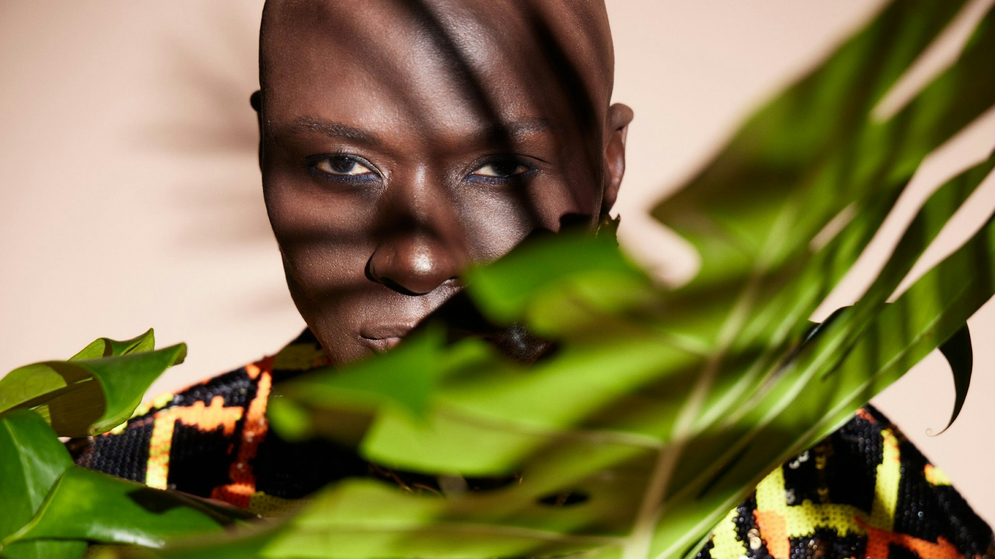 Papis Loveday blickt hinter Palmen in die Kameras von „Ich bin ein Star – Holt mich hier raus!“.