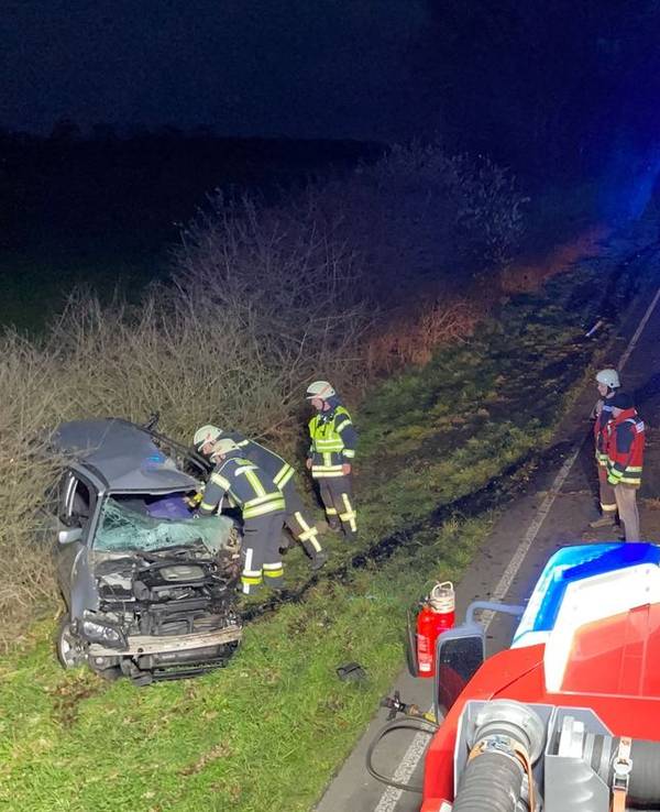 Ein Auto steht schwer beschädigt neben der Straße, mehrere Einsatzkräfte stehen davor. Auf der Straße befinden sich mehrere Einsatzfahrzeuge.