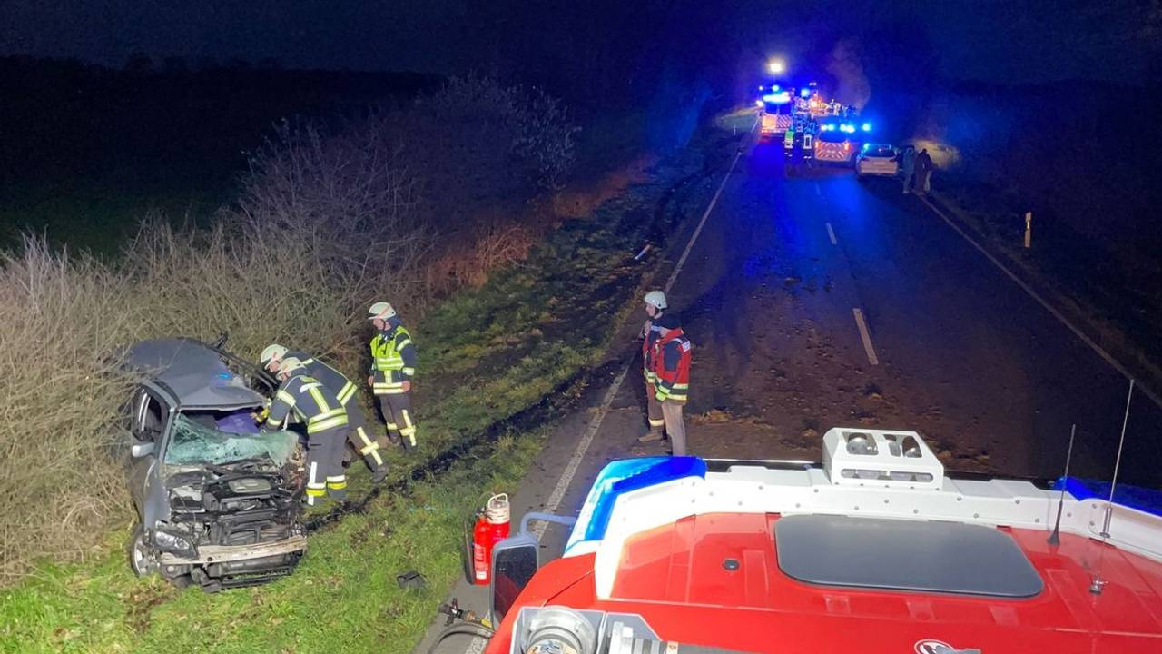 Ein Auto steht schwer beschädigt neben der Straße, mehrere Einsatzkräfte stehen davor. Auf der Straße befinden sich mehrere Einsatzfahrzeuge.