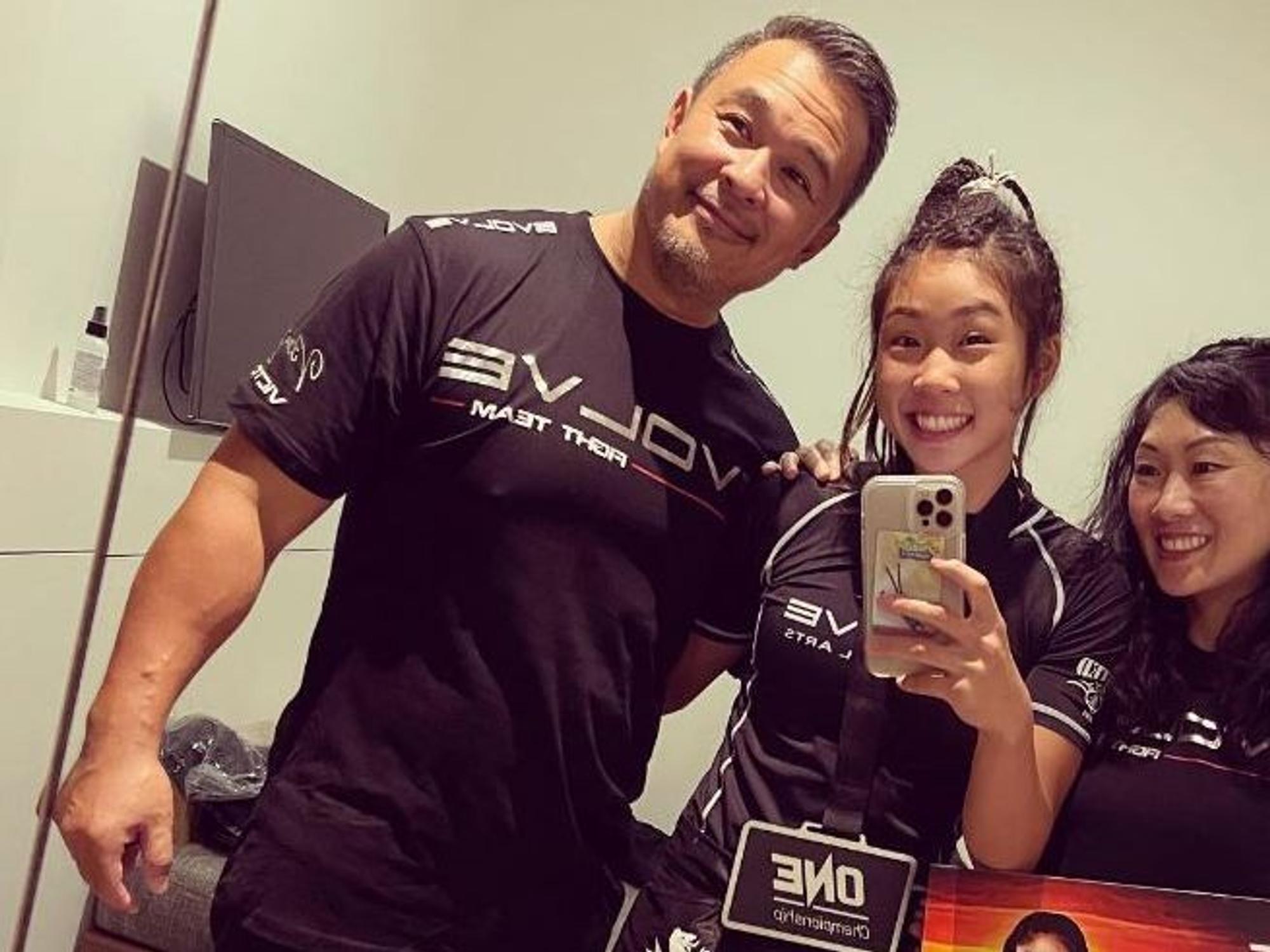 Victoria Lee (mitte) steht zwischen ihren Eltern und lächelt auf einem Selfie in die Kamera.
