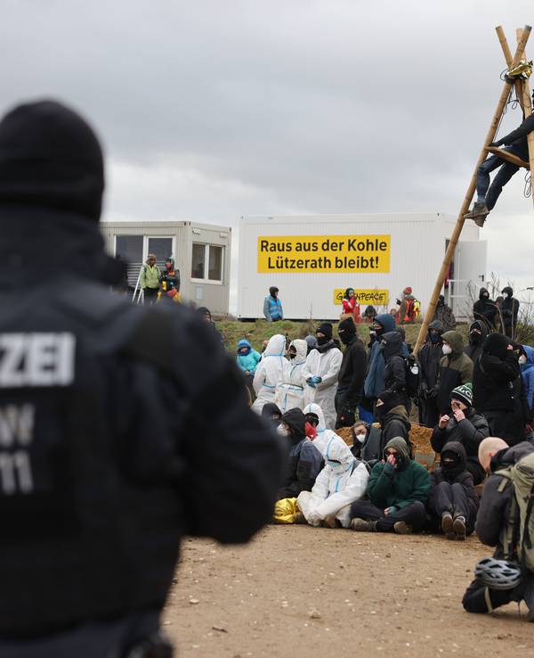 Ein Polizist beobachtet Klimaschutzaktivistinnen und -aktivisten, die am Rand des Tagebaus sitzen. Das Dorf Lützerath soll zur Erweiterung des Braunkohletagebaus Garzweiler II abgebaggert werden.