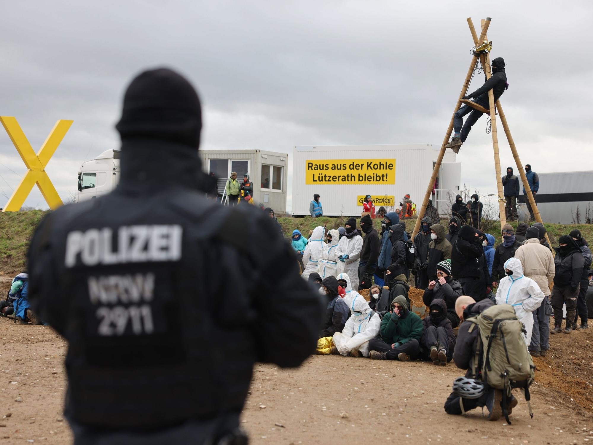 Ein Polizist beobachtet Klimaschutzaktivistinnen und -aktivisten, die am Rand des Tagebaus sitzen. Das Dorf Lützerath soll zur Erweiterung des Braunkohletagebaus Garzweiler II abgebaggert werden.