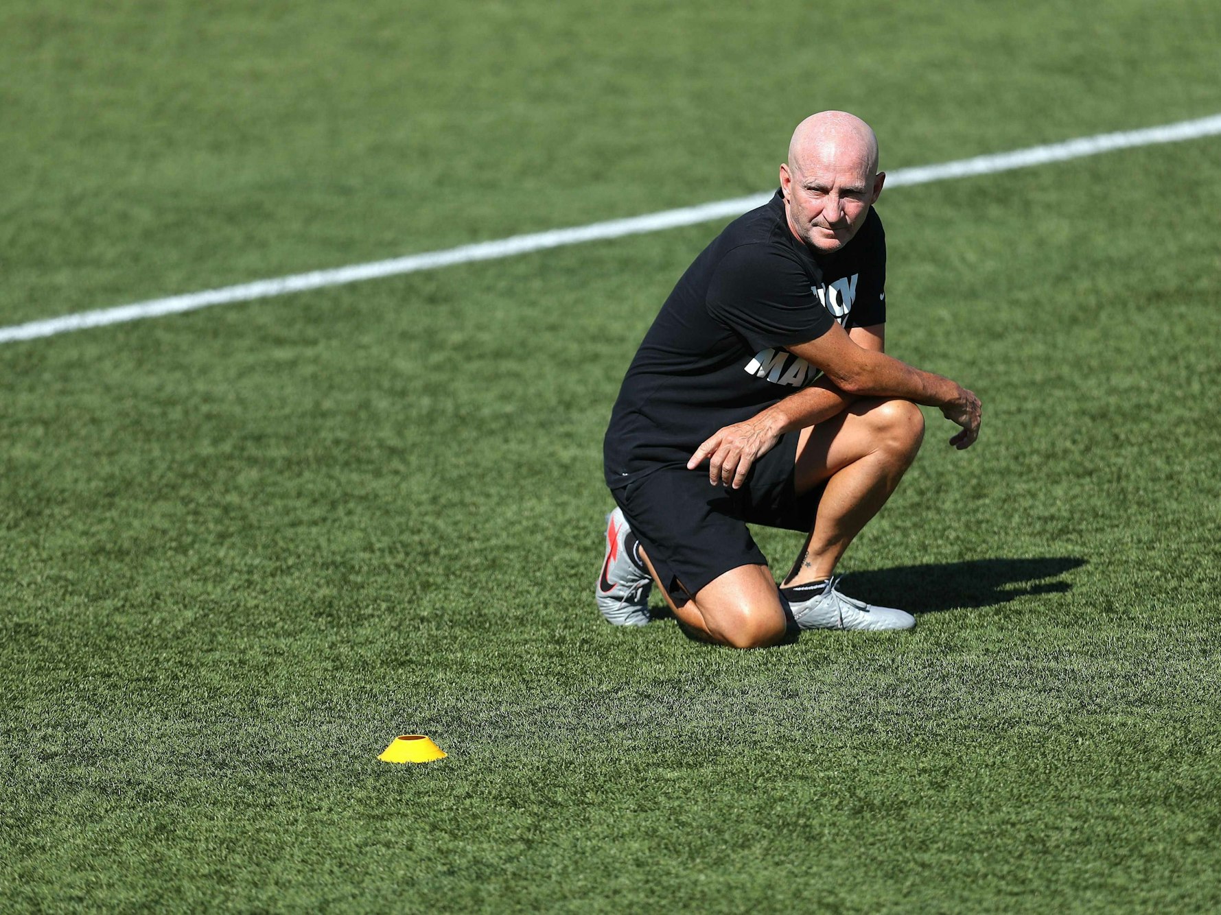 Frauenfußball-Trainer Paul Riley hockt auf dem Rasen.