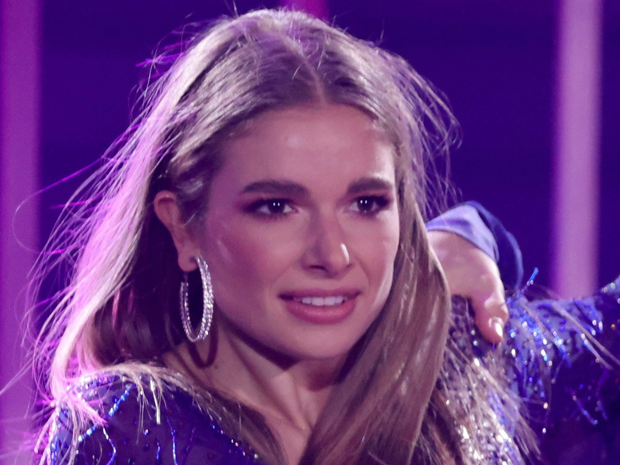 Lola Weippert trägt ein lilafarbenes Kostüm und schaut lächelnd in die Ferne.