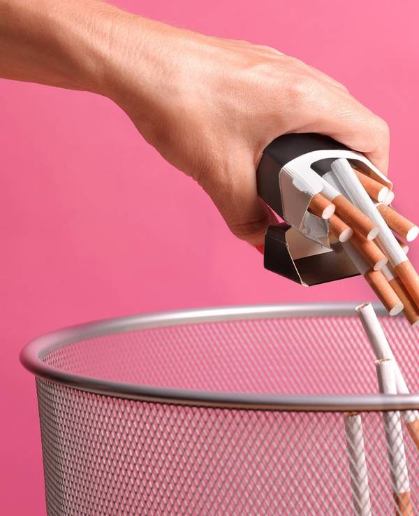 Eine Person schmeißt eine Zigarettenpackung samt Inhalt in einen Papierkorb.