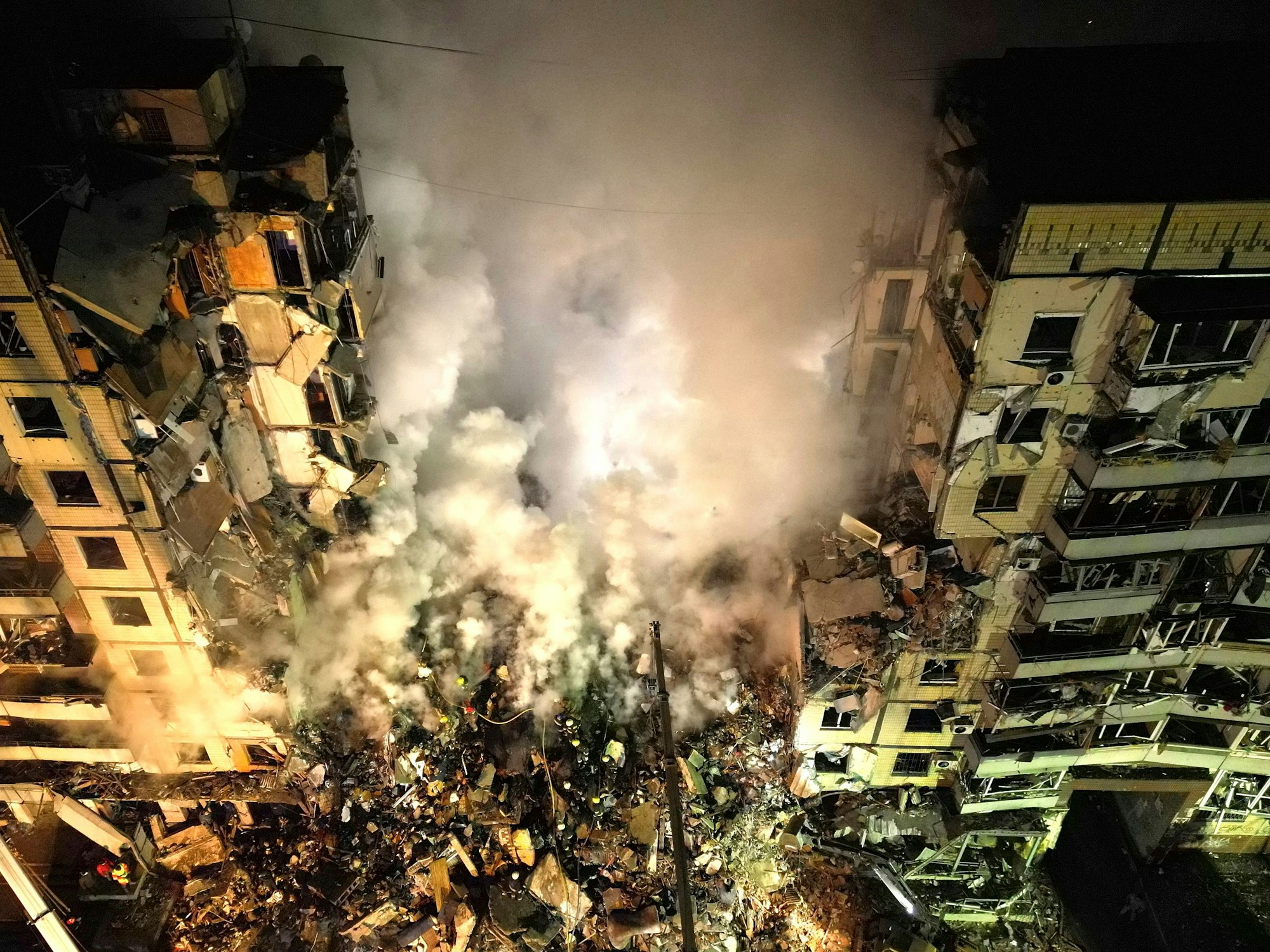 Rettungskräfte räumen Trümmer weg, nachdem eine russische Rakete nach ukrainischen Angaben in ein Hochhaus eingeschlagen ist. Bei dem Raketenangriff vom Samstag, 14. januar 2023, sind nach vorläufigen Behördenangaben mehrere Menschen getötet und viele weitere verletzt worden.