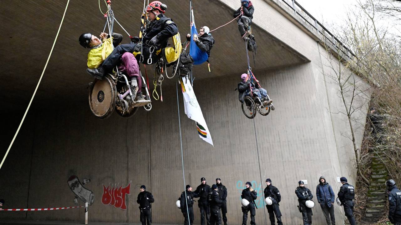 Ein Höhenretter der Polizei hilft einem Umweltaktivisten im Rollstuhl auf den Boden.