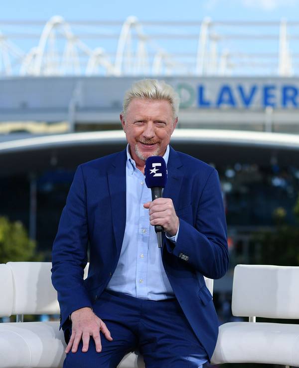 Boris Becker sitzt mit einem Eurosport-Mikrofon in der Hand auf einem Sofa.