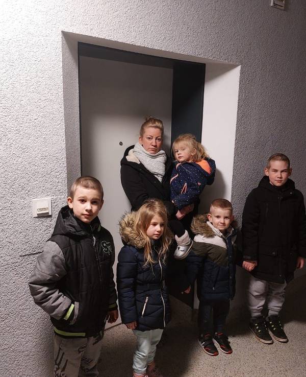 Eine Frau steht mit ihren Kindern vor einer Tür.