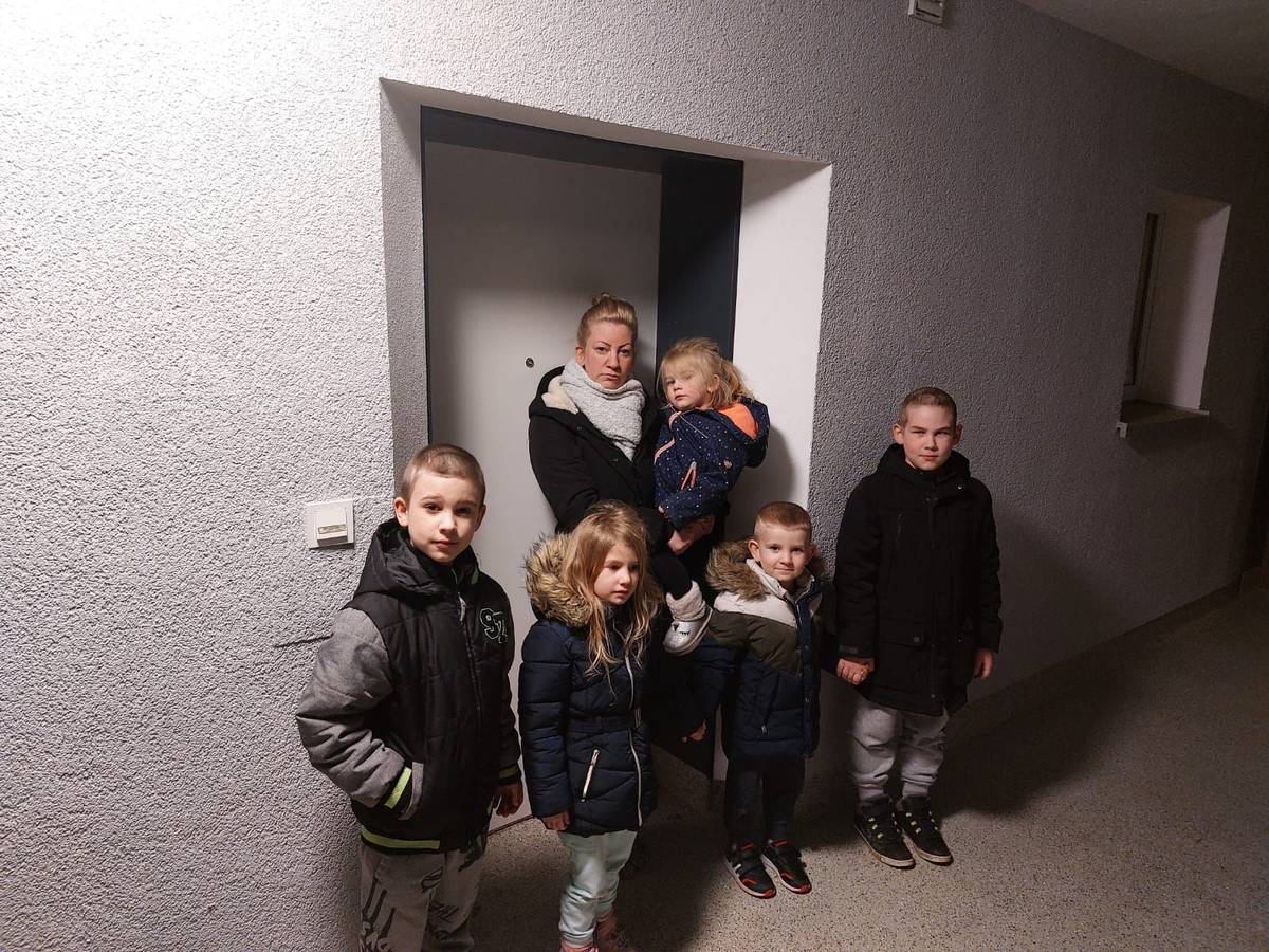 Eine Frau steht mit ihren Kindern vor einer Tür.