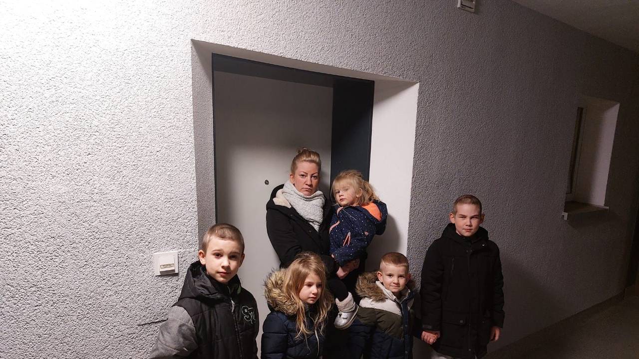 Eine Frau steht mit ihren Kindern vor einer Tür.