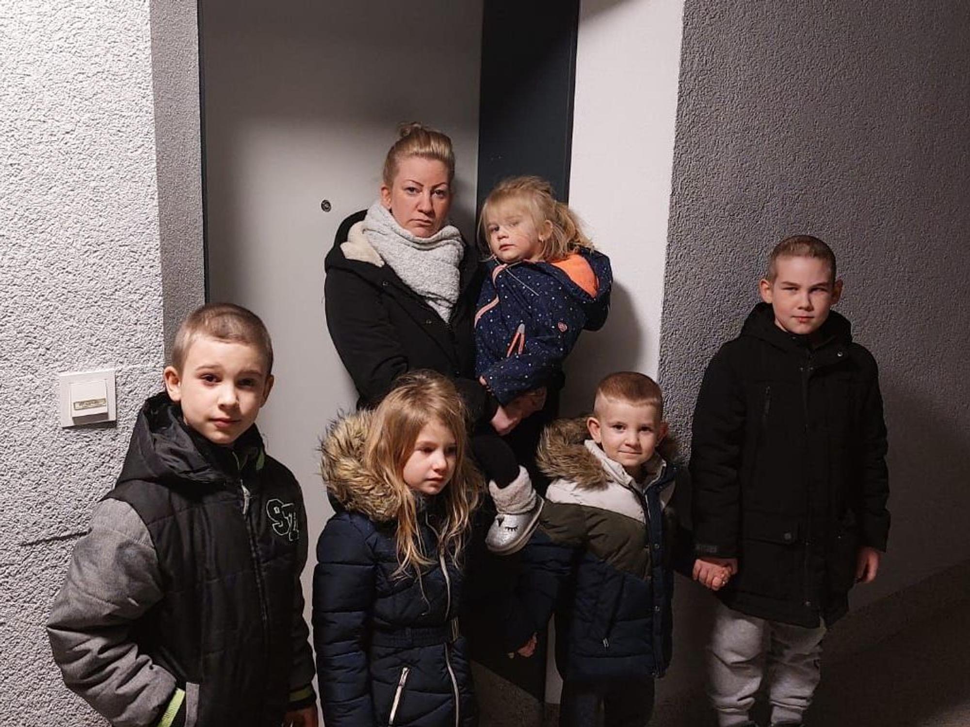 Eine Frau steht mit ihren Kindern vor einer Tür.