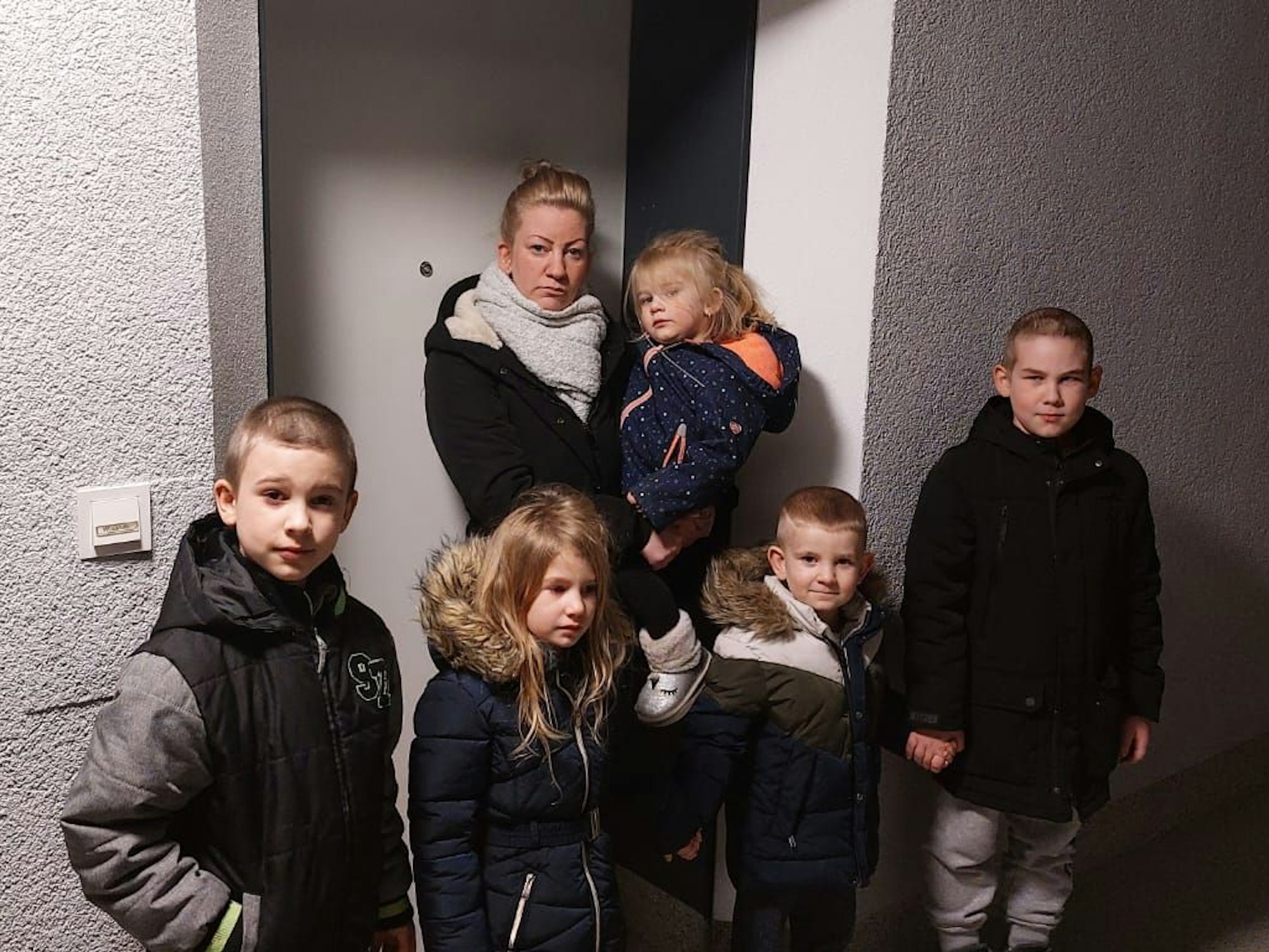 Eine Frau steht mit ihren Kindern vor einer Tür.
